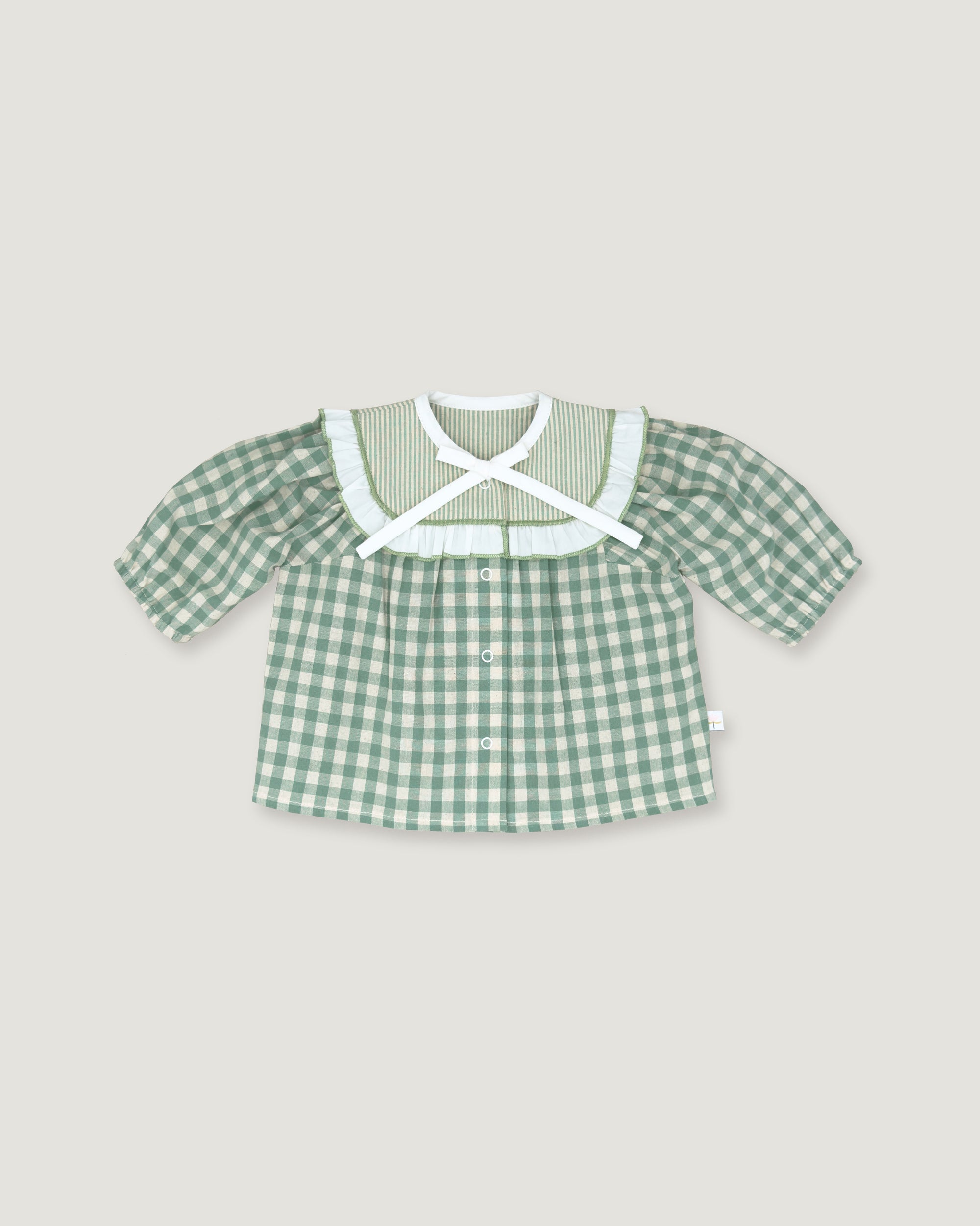 A baby girl's short-sleeve button-up shirt in a green and white gingham check pattern, featuring a wide white ruffled collar with a white cross-front bow, displayed flat against a light beige background.
