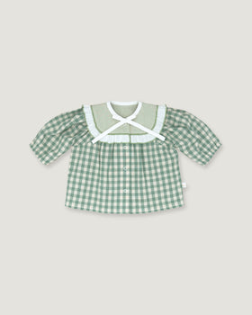 A baby girl's short-sleeve button-up shirt in a green and white gingham check pattern, featuring a wide white ruffled collar with a white cross-front bow, displayed flat against a light beige background.