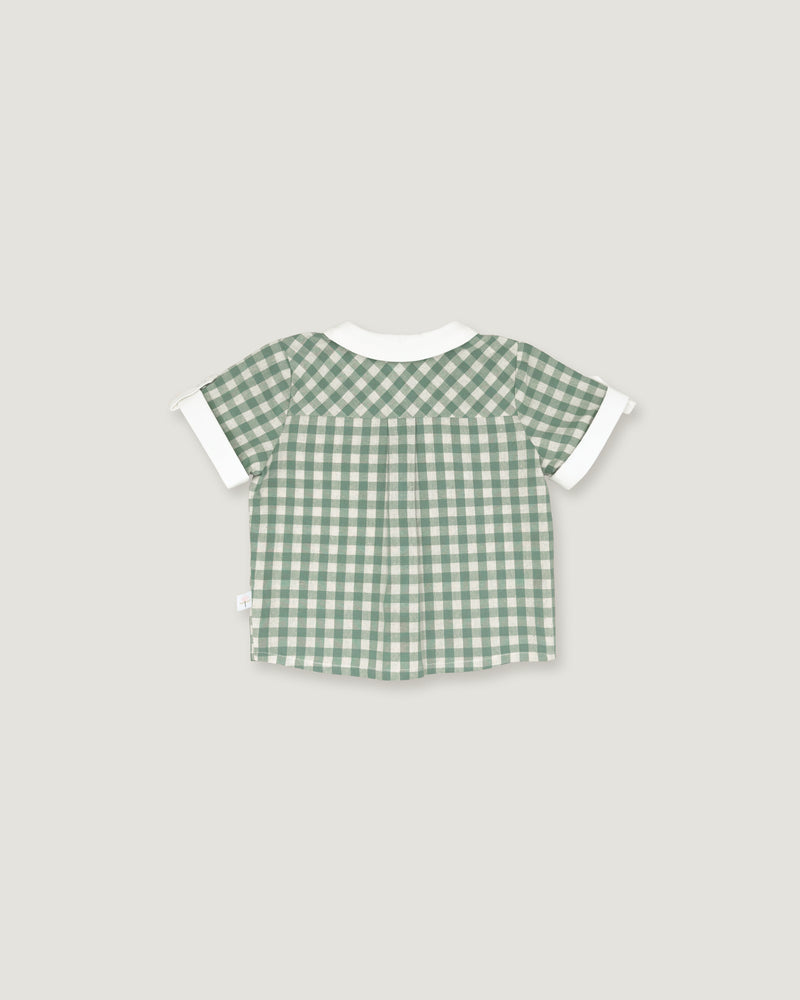 A short-sleeve baby top with a green and white gingham check pattern, featuring solid white ruffle trim at the collar and sleeve cuffs, shown against a light gray background.