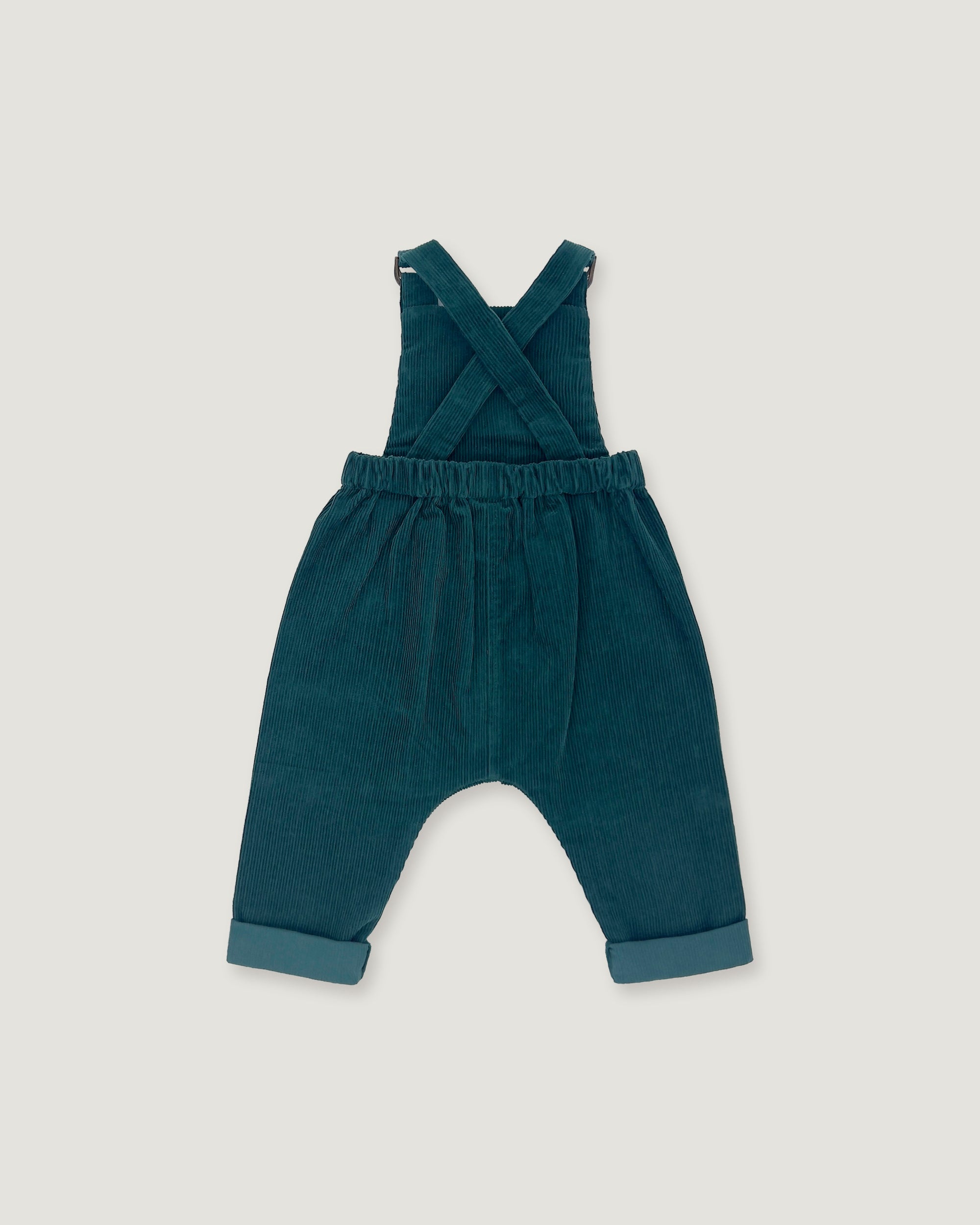 A pair of toddler corduroy overall jumpsuit in a deep teal blue-green color, featuring adjustable shoulder straps that cross over the chest and cuffed harem-style legs, shown flat on a light gray background.
