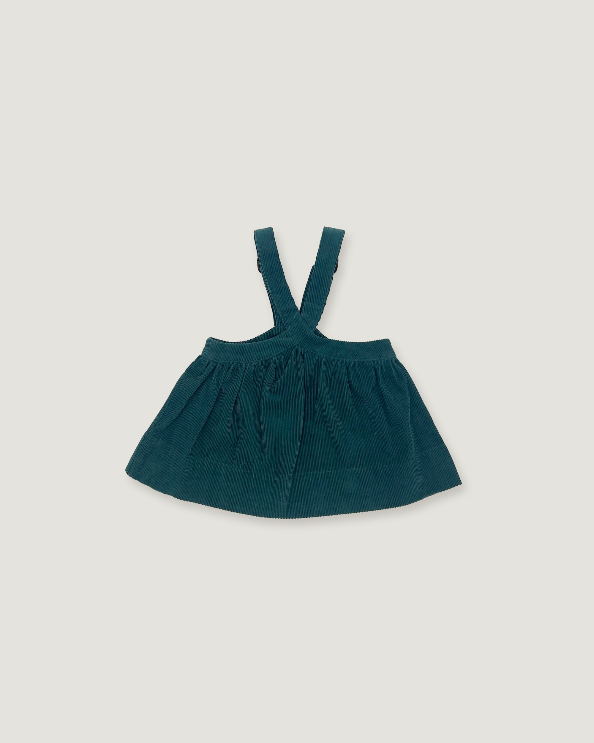 A dark teal corduroy baby dress with shoulder straps, laid flat on a light gray background.