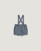 A pair of baby boy's denim bib shorts with adjustable shoulder straps and two brown buttons, laid flat on a light beige background.