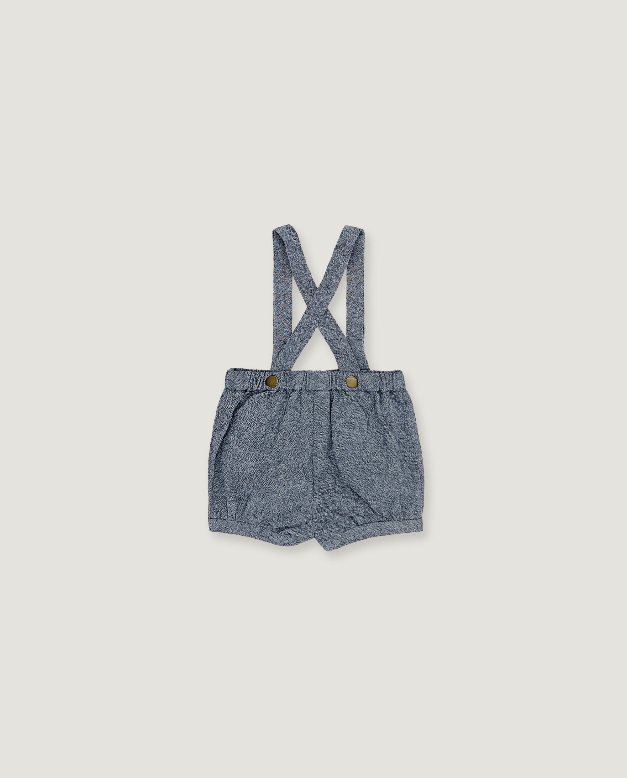 A pair of baby boy's denim bib shorts with adjustable shoulder straps and two brown buttons, laid flat on a light beige background.