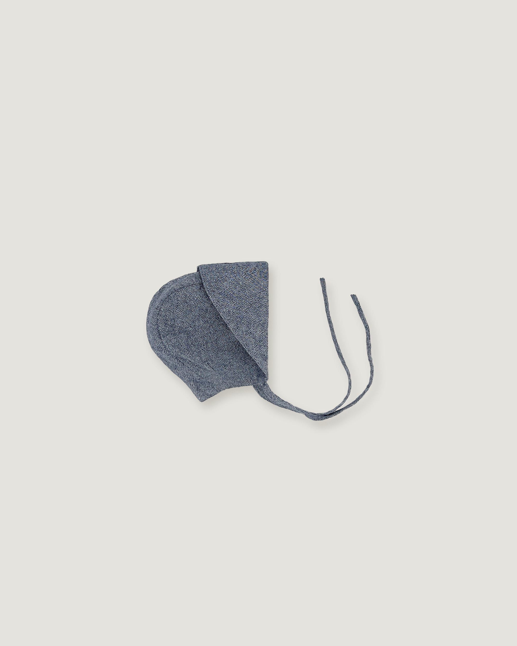 A denim blue linen bonnet with a long visor rolled up  on a white background