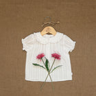 White blouse with floral design on a hanger against a brown textured background