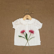 White blouse with floral design on a hanger against a brown textured background