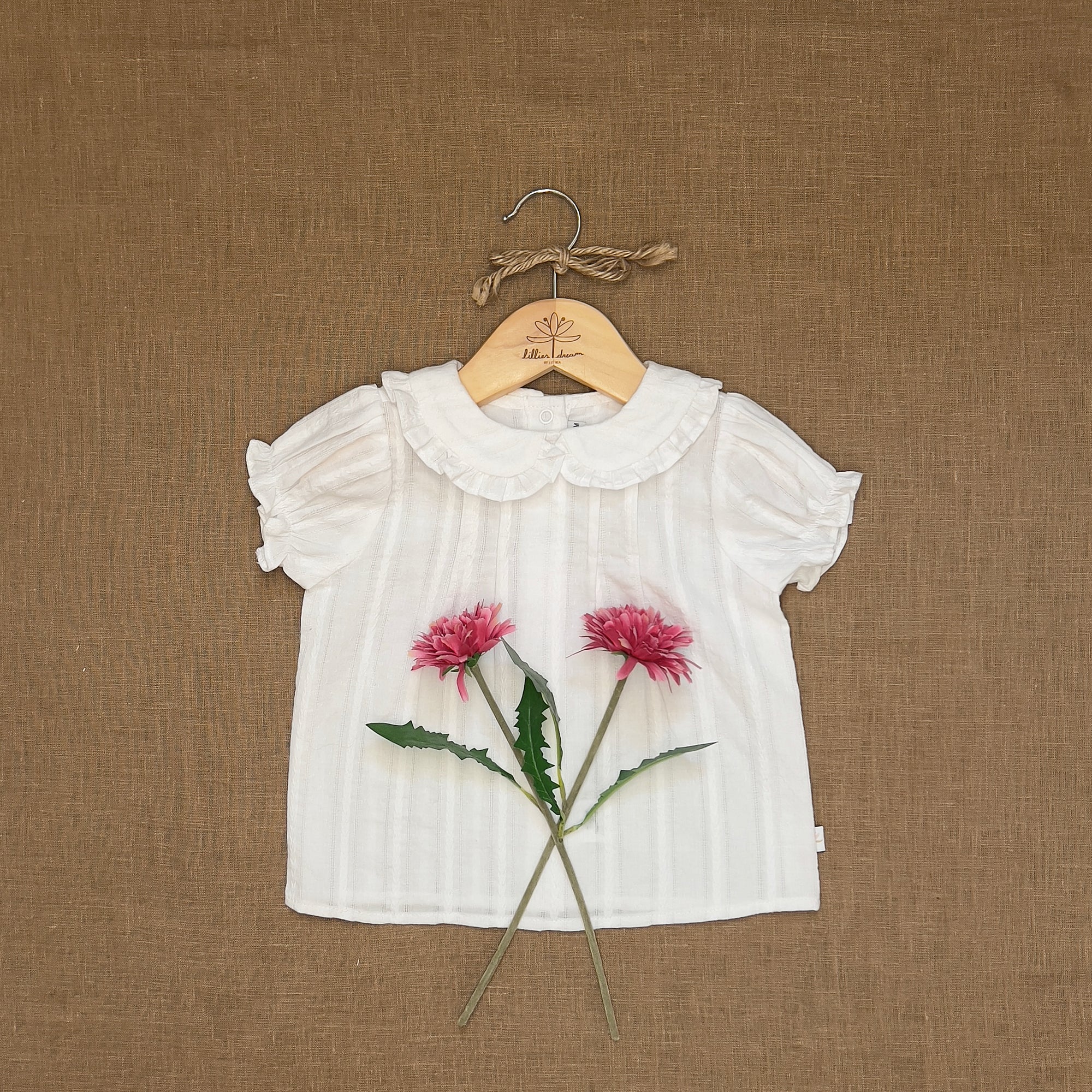 White blouse with floral design on a hanger against a brown textured background