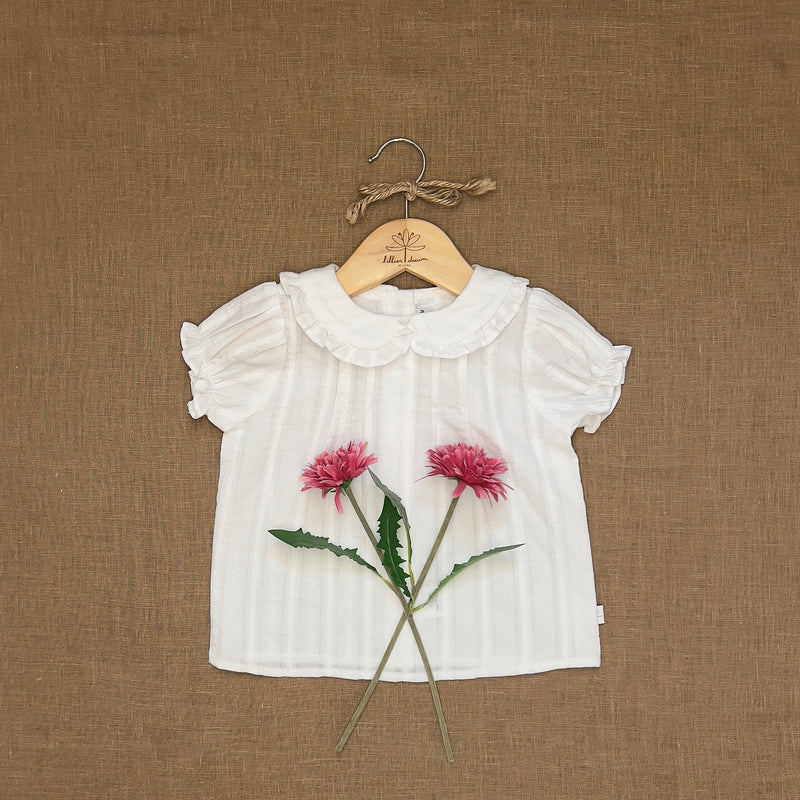 White blouse with floral design on a hanger against a brown textured background