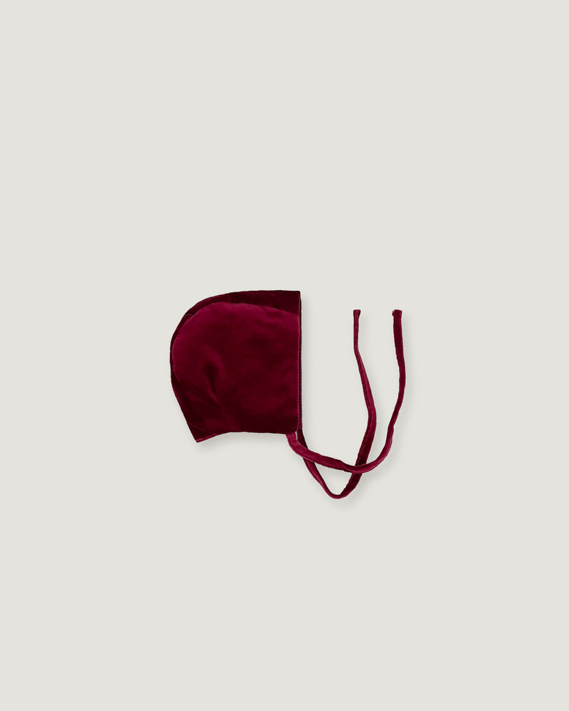 A burgundy velvet bonnet with thin matching tie strings, laid flat on a light gray background.