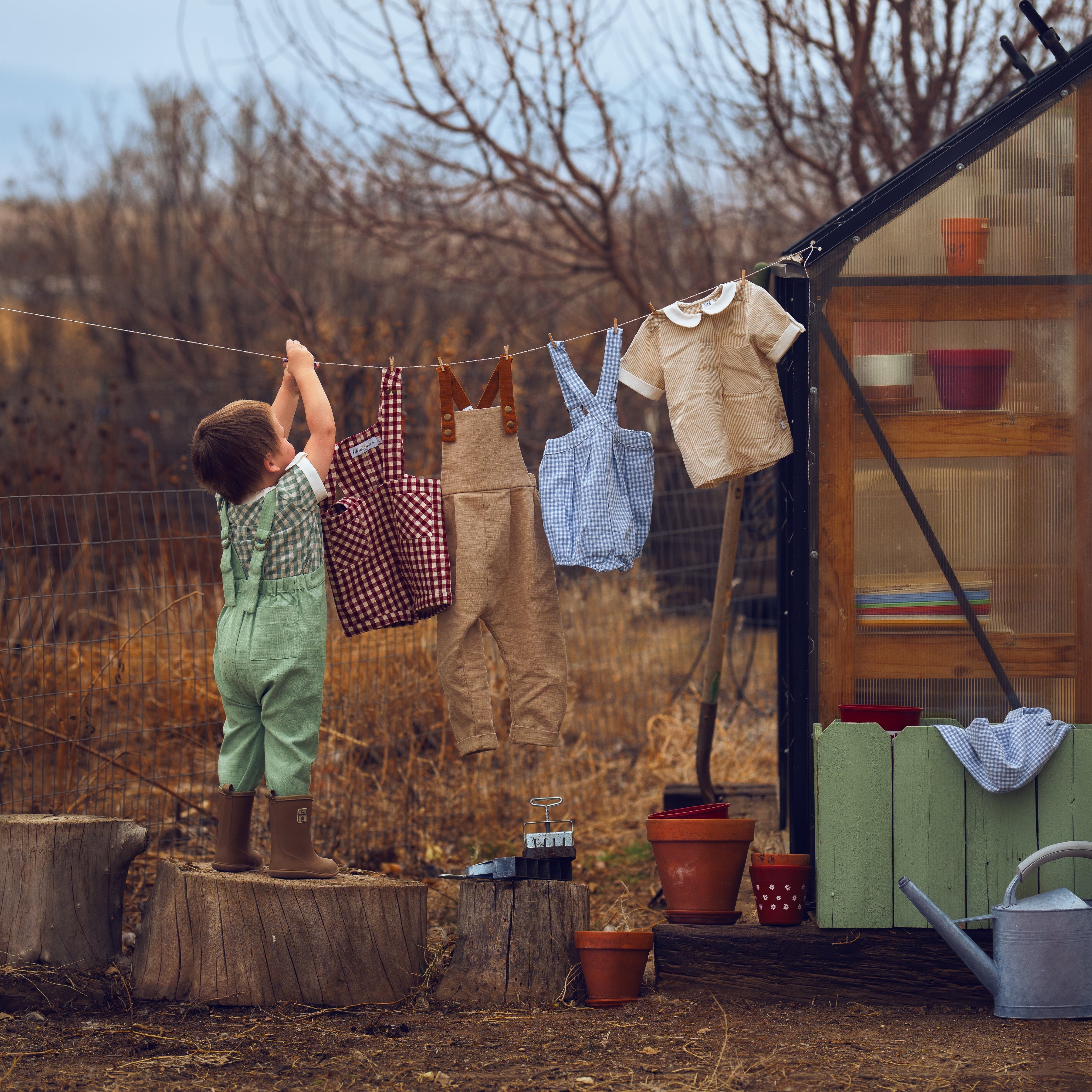 Child hanging clothes on a line outdoors with a shed and garden tools in the background