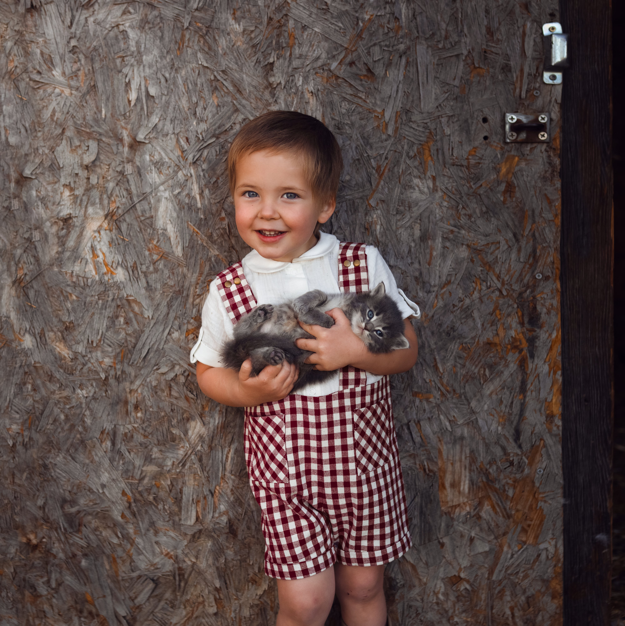 Child holding two cats in front of a rustic wooden wall