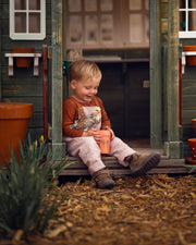 little boy in checkered overalls in a barn with birds