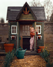 little boy in checkered overalls  standing in  front of a toy  barn