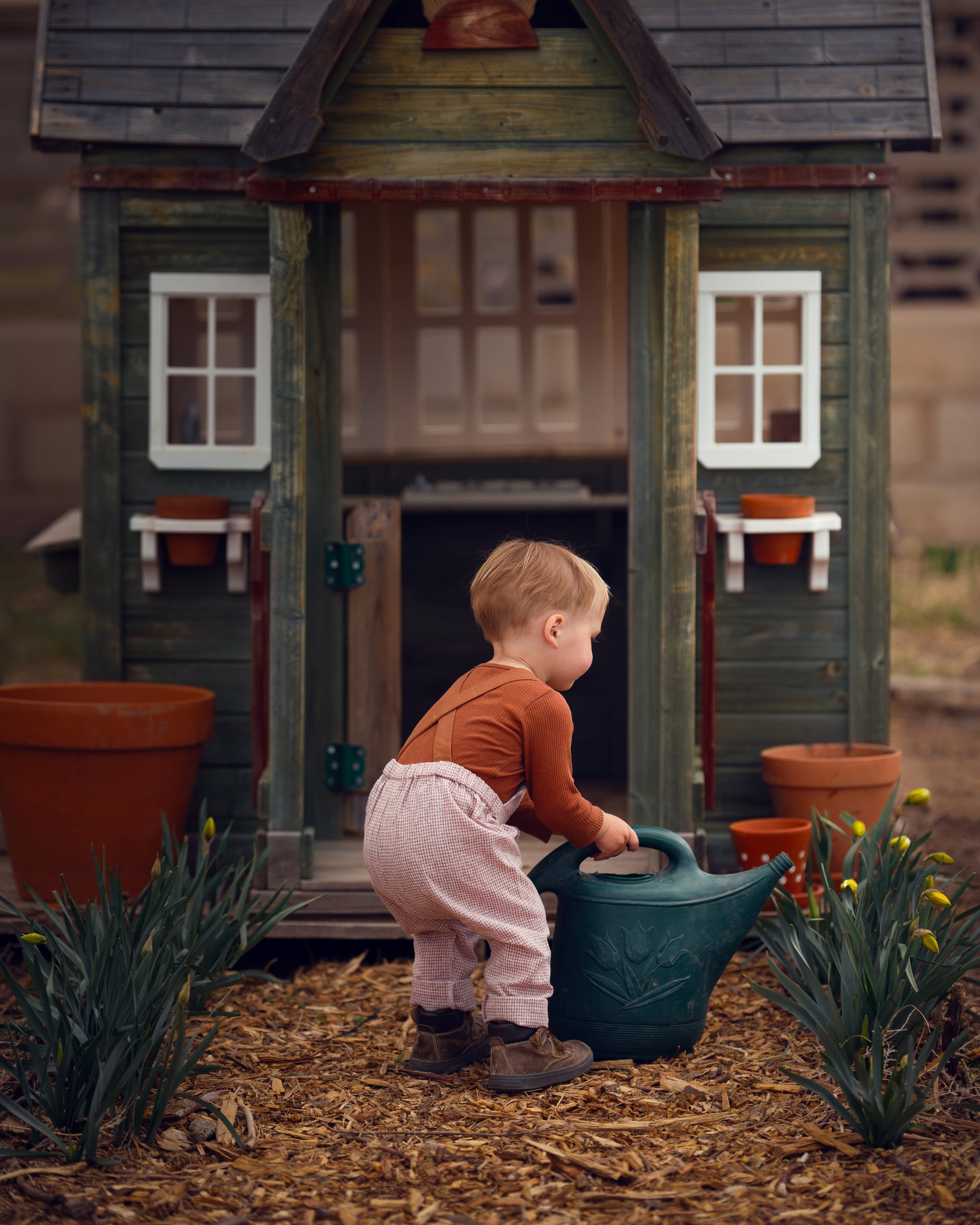 little boy in checkered overalls in front of a barn