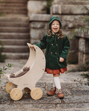 Child in a green coat and hat holding a wooden toy outdoors.