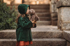 Child in a green coat holding a teddy bear on stone steps