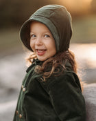 Smiling 3-year-old girl wearing the Evergreen corduroy bonnet and matching coat, highlighting the gender-neutral style and comfortable fit.