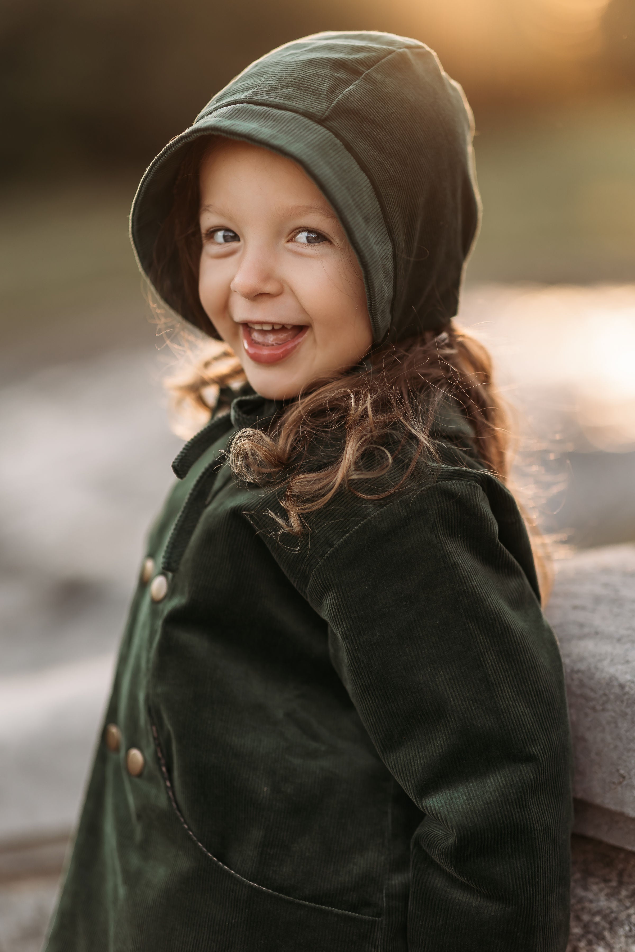 Smiling 3-year-old girl wearing the Evergreen corduroy bonnet and matching coat, highlighting the gender-neutral style and comfortable fit.