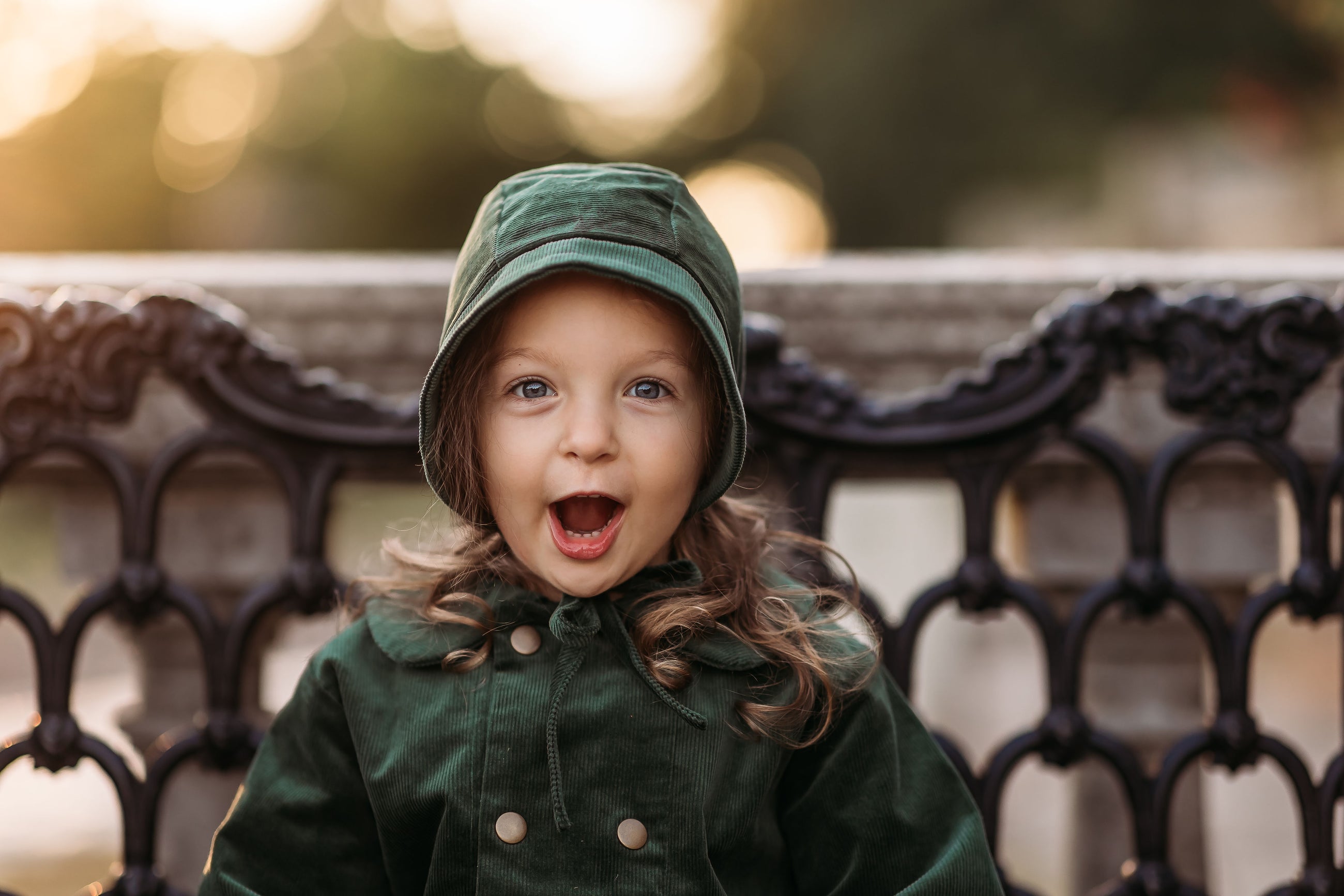 Child wearing a green coat and hat with a blurred background