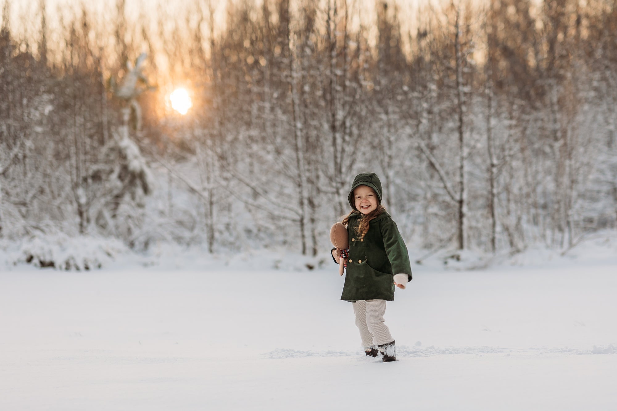 Three-year-old girl in a white, snowy field wearing the Evergreen bonnet and matching corduroy coat, epitomizing natural, eco-friendly fashion for kids.