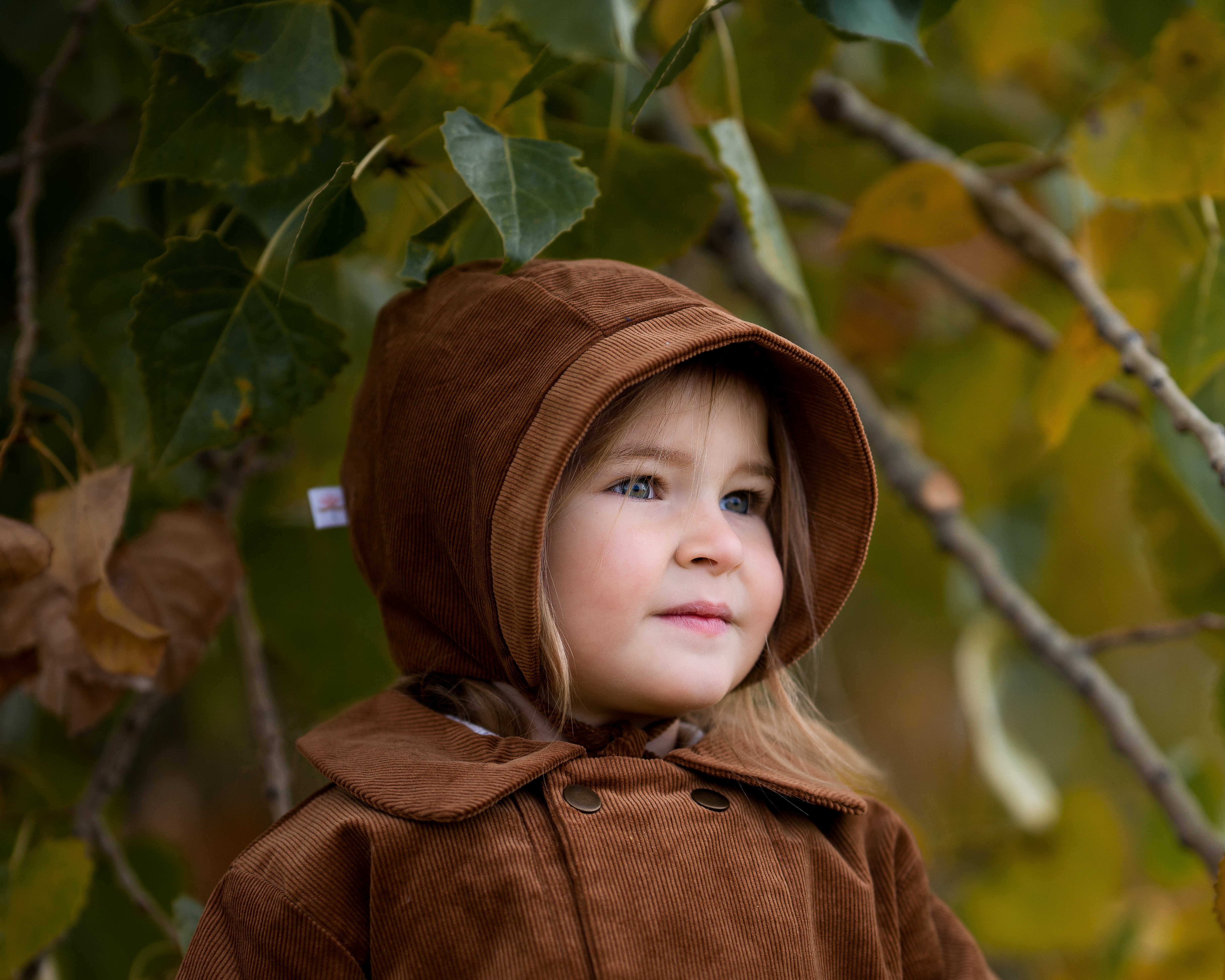 Model girl wearing the Camel Bonnet, detail view - This close-up shot focuses on the bonnet’s fabric and lining, emphasizing the coordinating brushed gingham cotton that adds comfort and warmth.