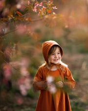 Girl in matching rust dress and bonnet smiling dreamily
