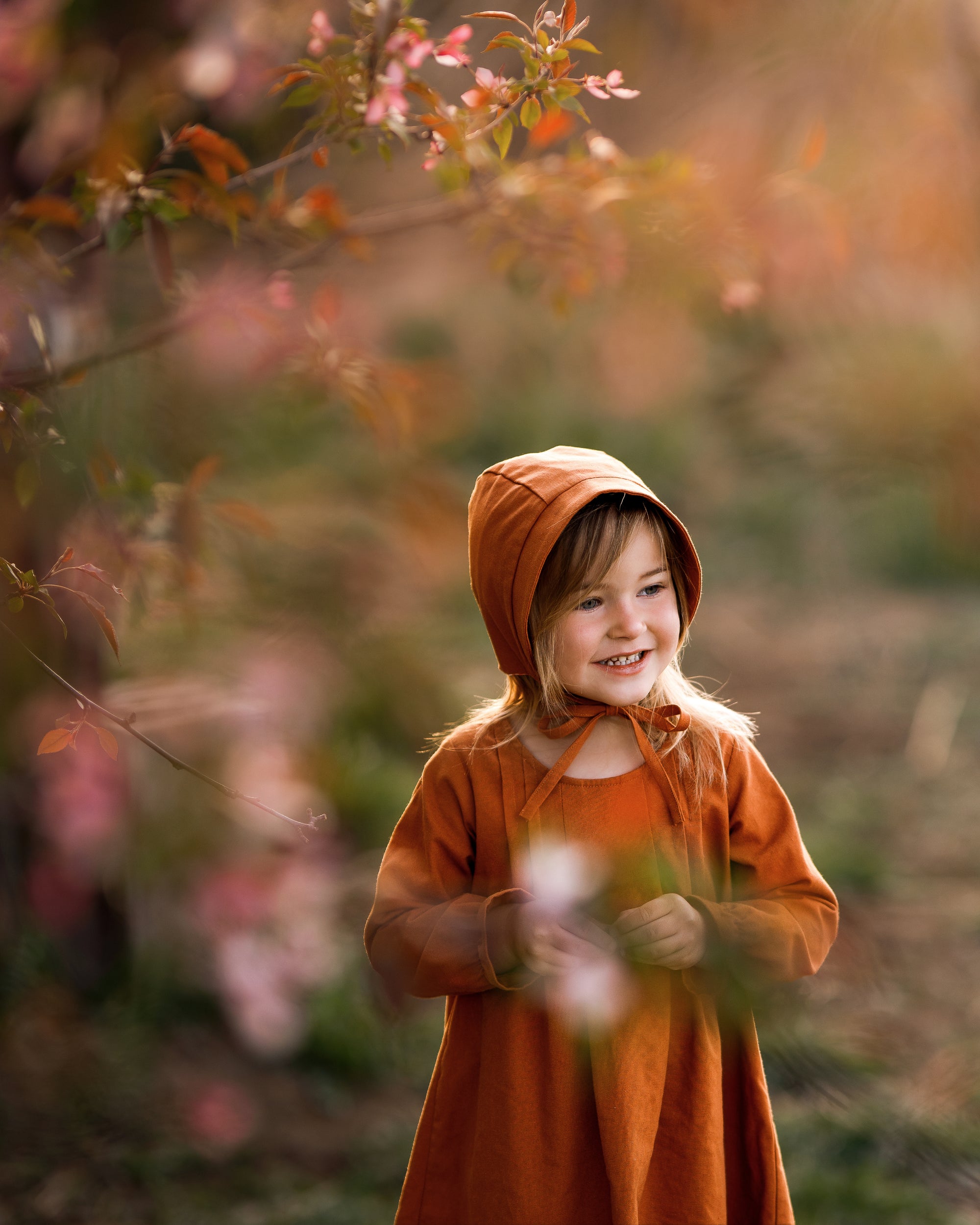 Girl in matching rust dress and bonnet smiling dreamily