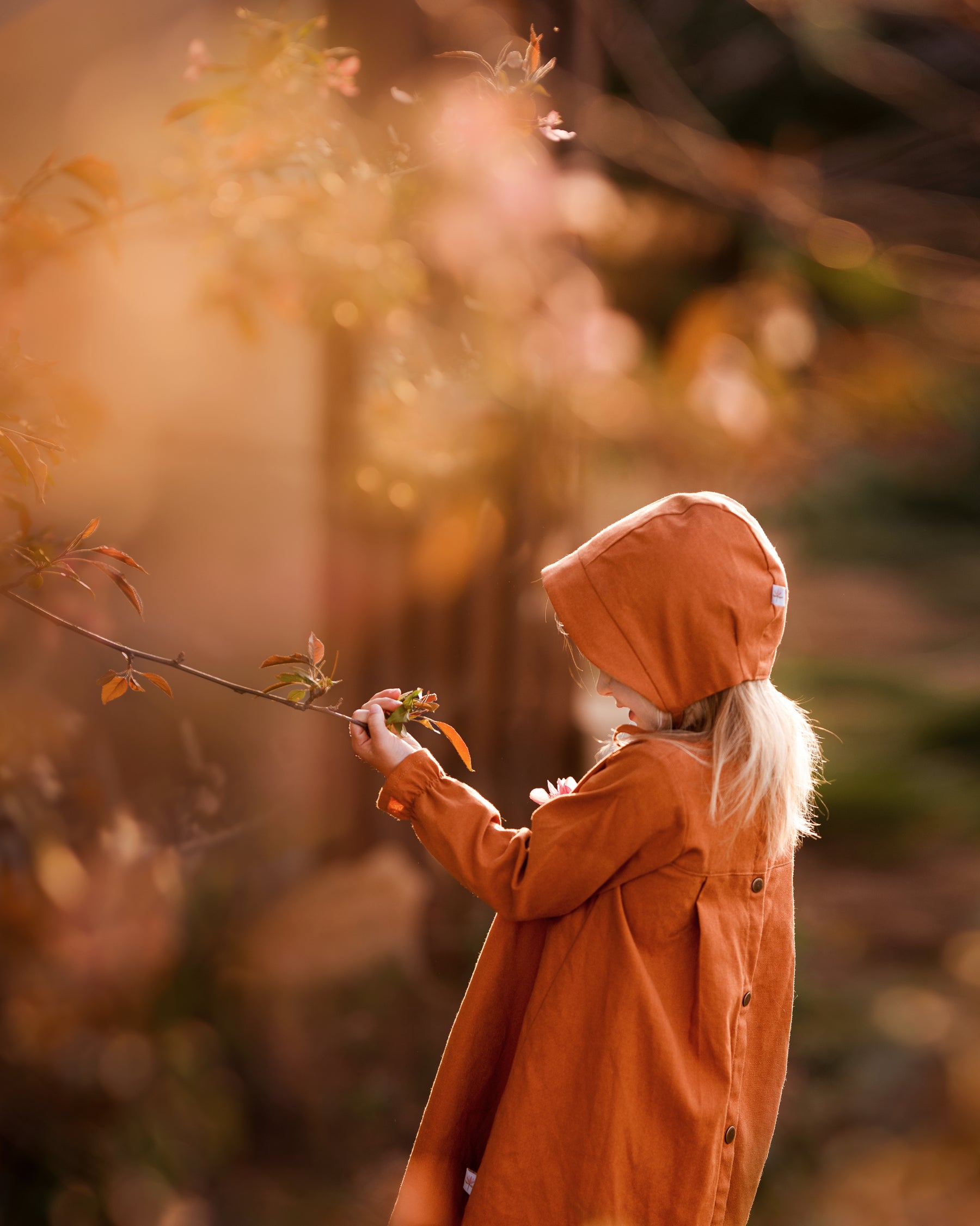 Girl in matching rust dress and bonnet looking at plants