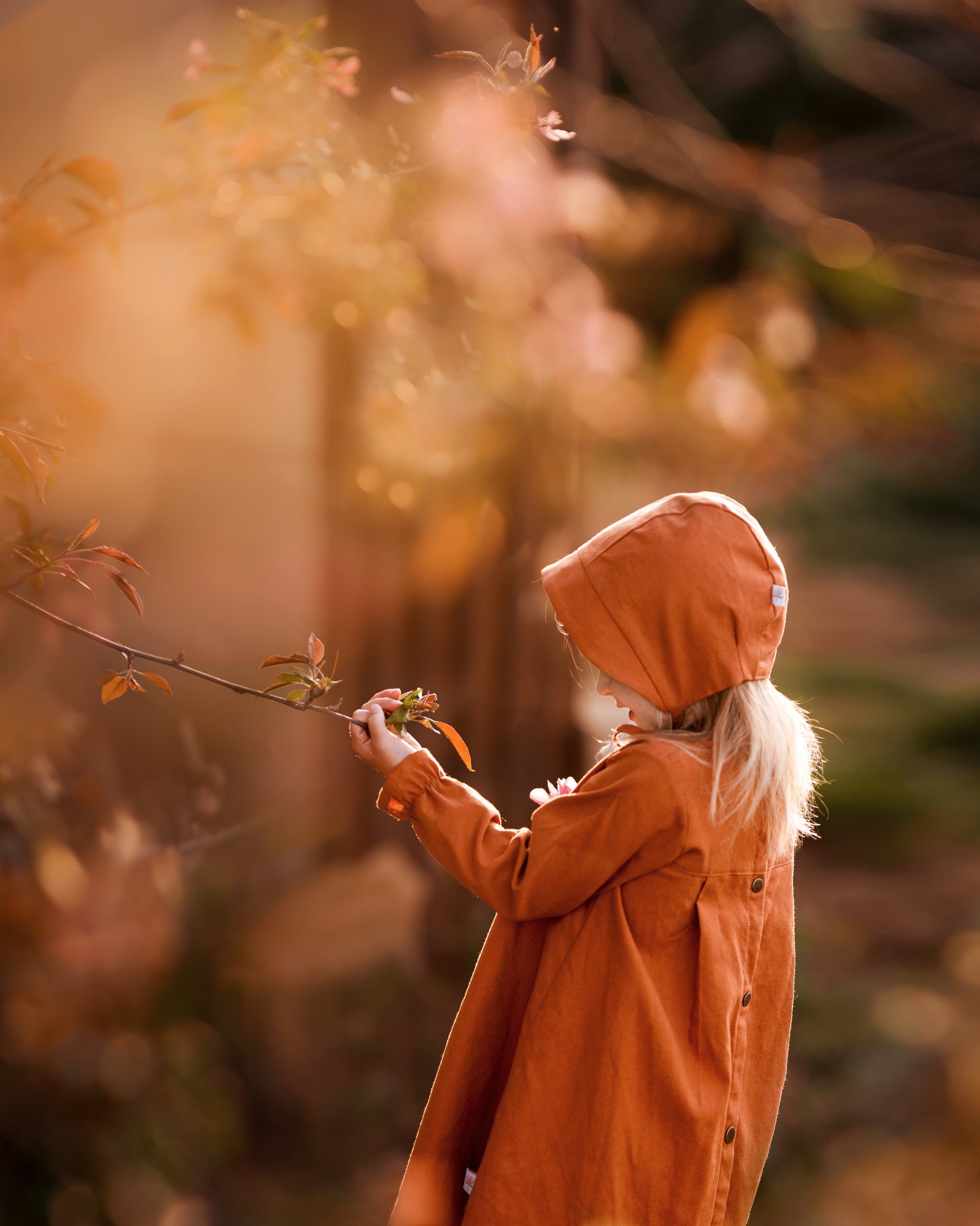 Girl in matching rust dress and bonnet looking at plants
