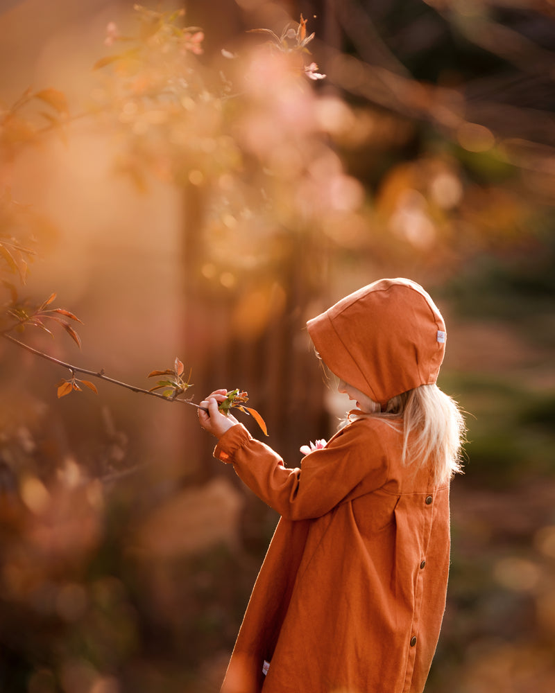 Girl in matching rust dress and bonnet looking at plants