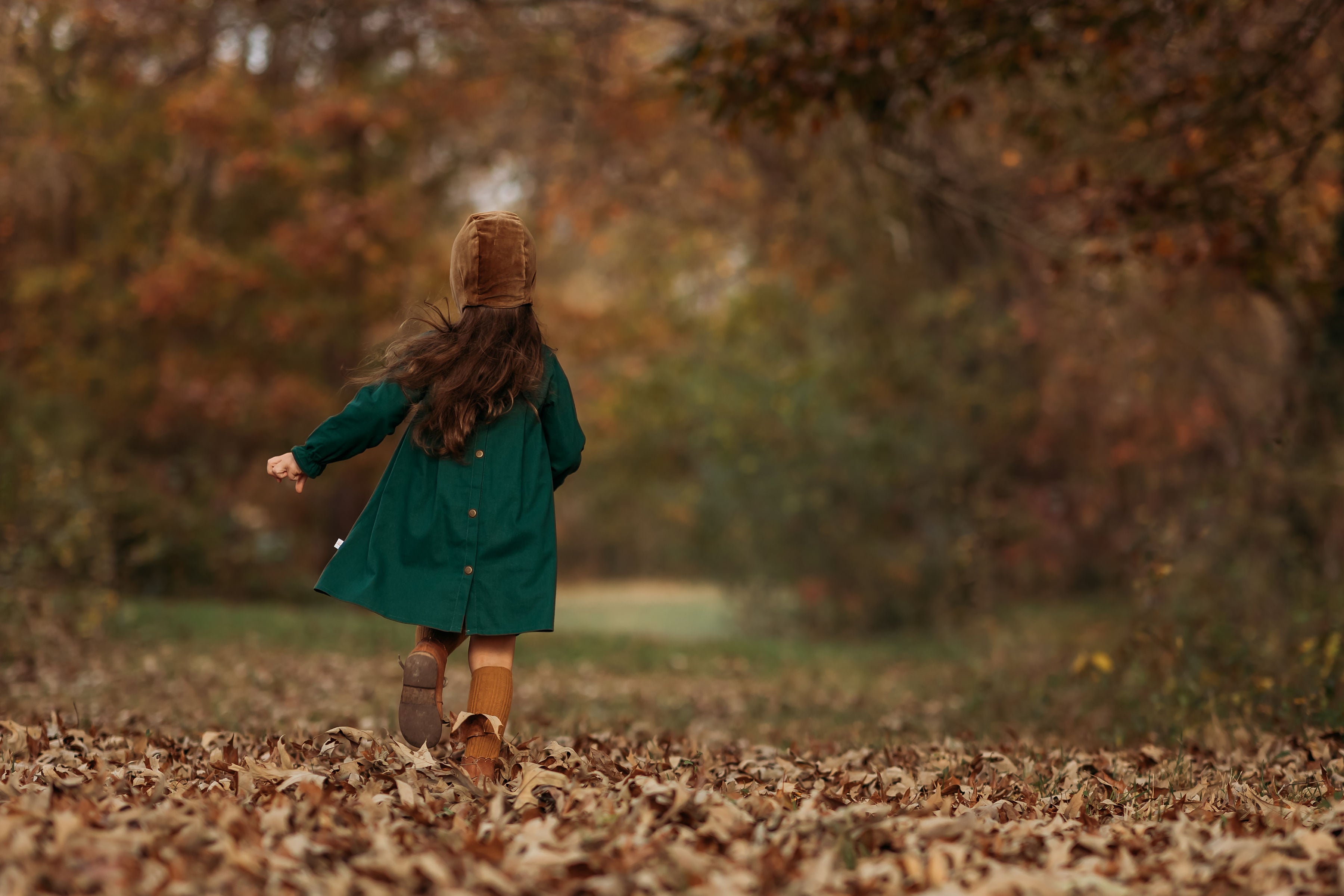 Back view of a 4-year-old girl running in the evergreen linen dress, illustrating the pleated back yoke that provides comfort and a stylish fit for active play.