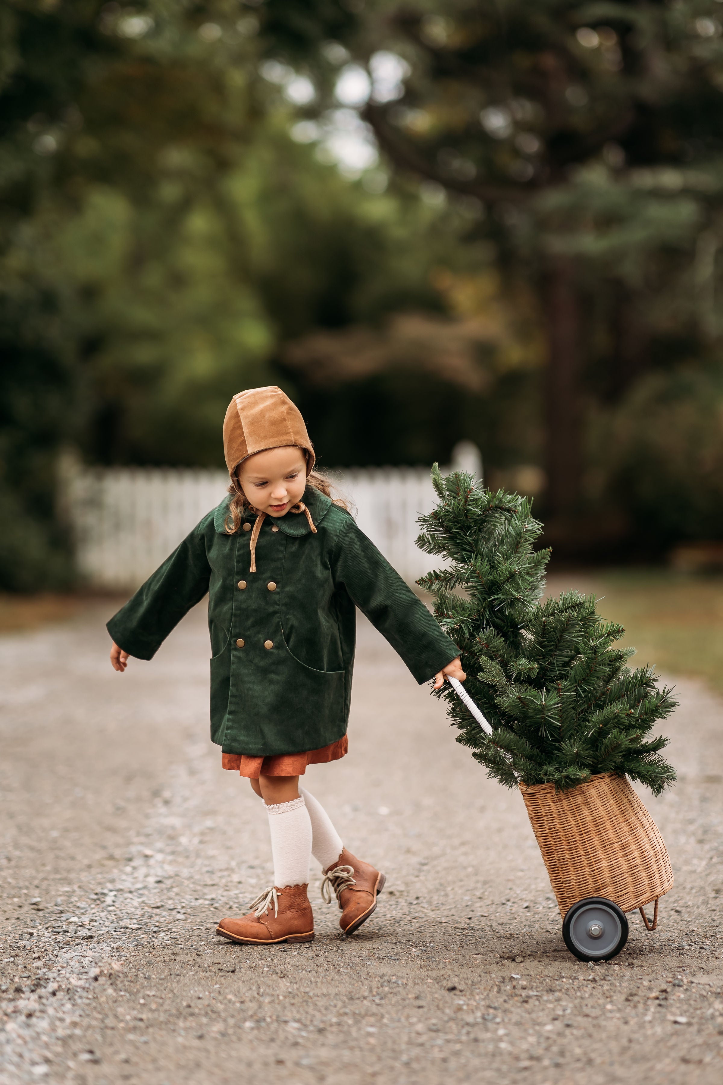 Model girl wearing the Gold Velvet Bonnet combined with our Evergreen Corduroy Coat, joyfully pulling a Christmas tree, showcasing the versatile design suitable for festive occasions.