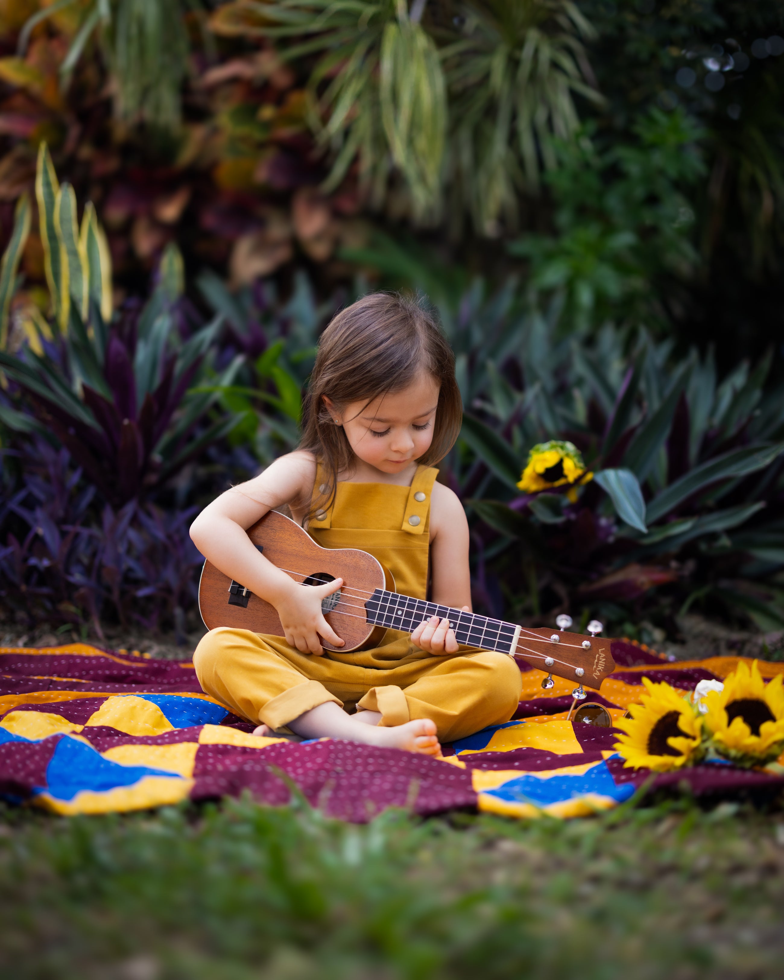 A 4-year-old girl playing ukulele freely in ginger long overalls, emphasizing the comfort and durability of the handmade 100% cotton fabric.