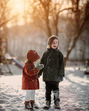 Boy and girl in matching green and rust coats in the snow smiling
