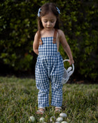 A little girl joyfully wearing Blue Gingham Linen Long Overalls, showcasing the playful and gender-neutral design perfect for Easter celebrations. The breathable fabric keeps her comfortable, while stylish pleats add a charming touch. The durable leather-looking straps and adjustable fit ensure she looks adorable and feels great during her festive activities.