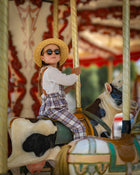 Child on a carousel with a horse, wearing a straw hat and sunglasses and plaid linen overalls.