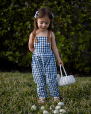 A little girl playfully sticking her tongue out while wearing Blue Gingham Linen Long Overalls, capturing a joyful moment during Easter. The gender-neutral design and breathable fabric allow for carefree movement, while the stylish pleats add a touch of elegance. Durable leather-looking straps and an adjustable fit make these overalls both fun and practical, reflecting the brand's commitment to sustainable fashion for children.