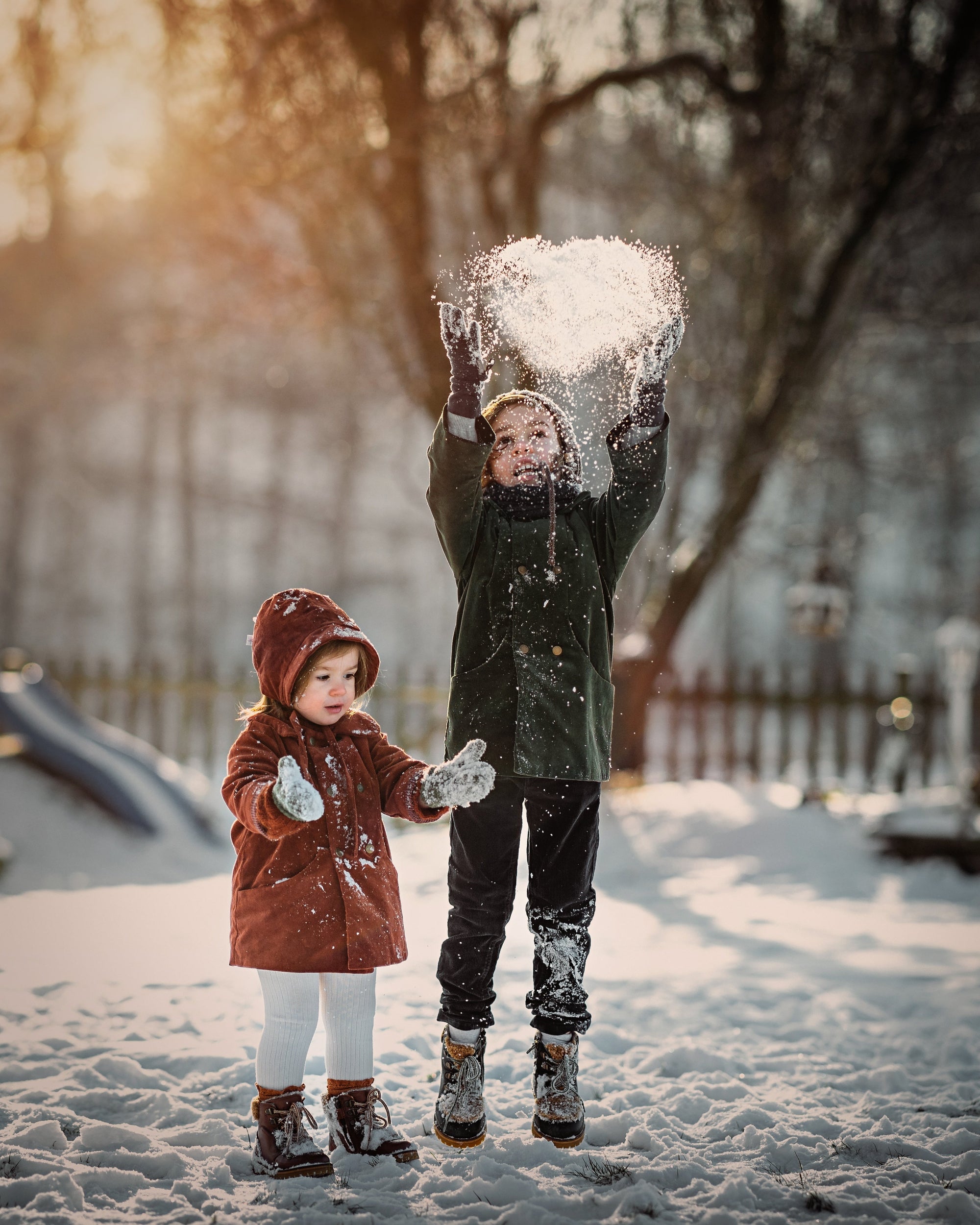 Boy and girl in matching green and rust coats playing in the snow