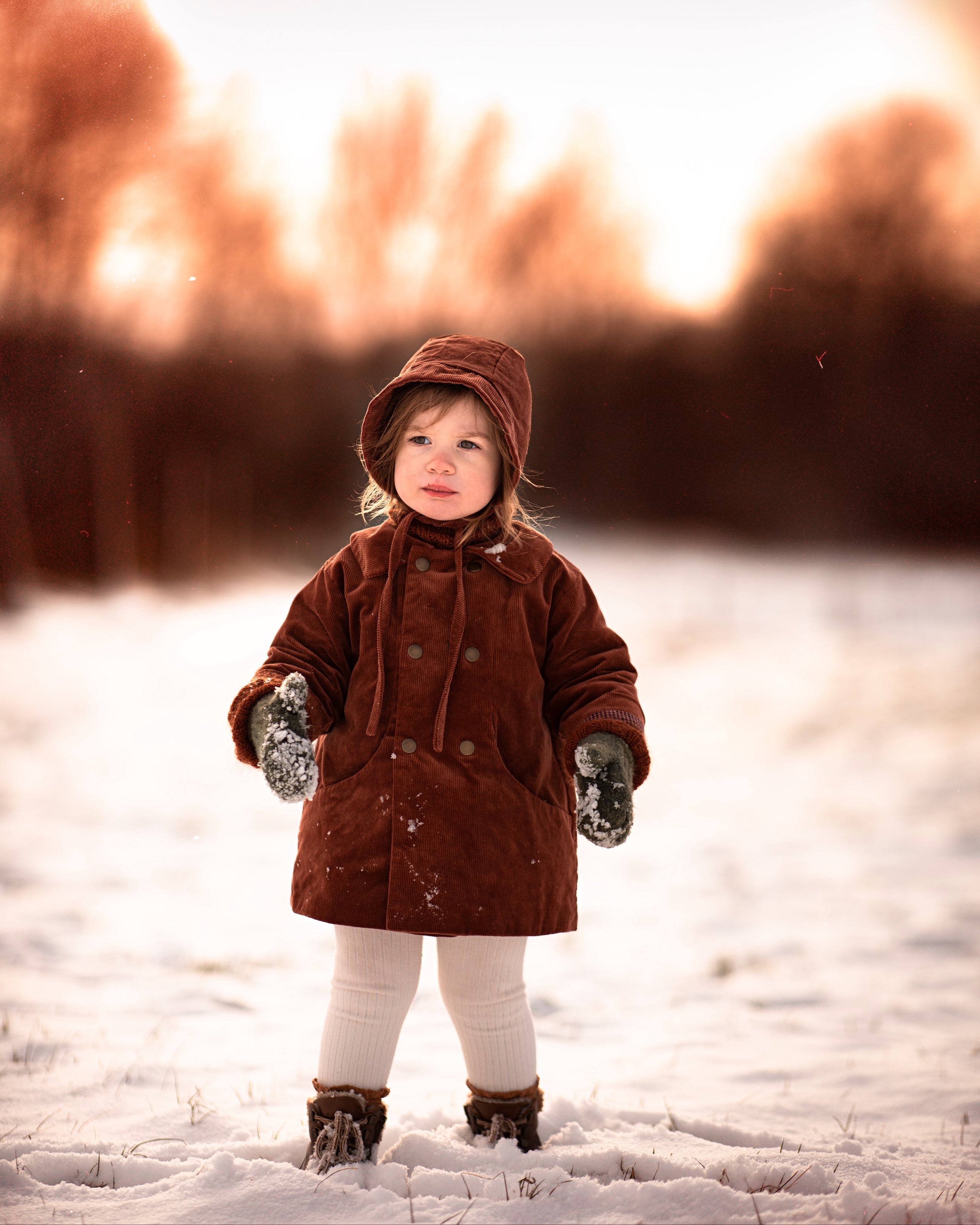 Little girl in the snow in a rust coat and matching hat with blurry background