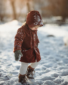Little girl in the snow in a rust coat and matching hat