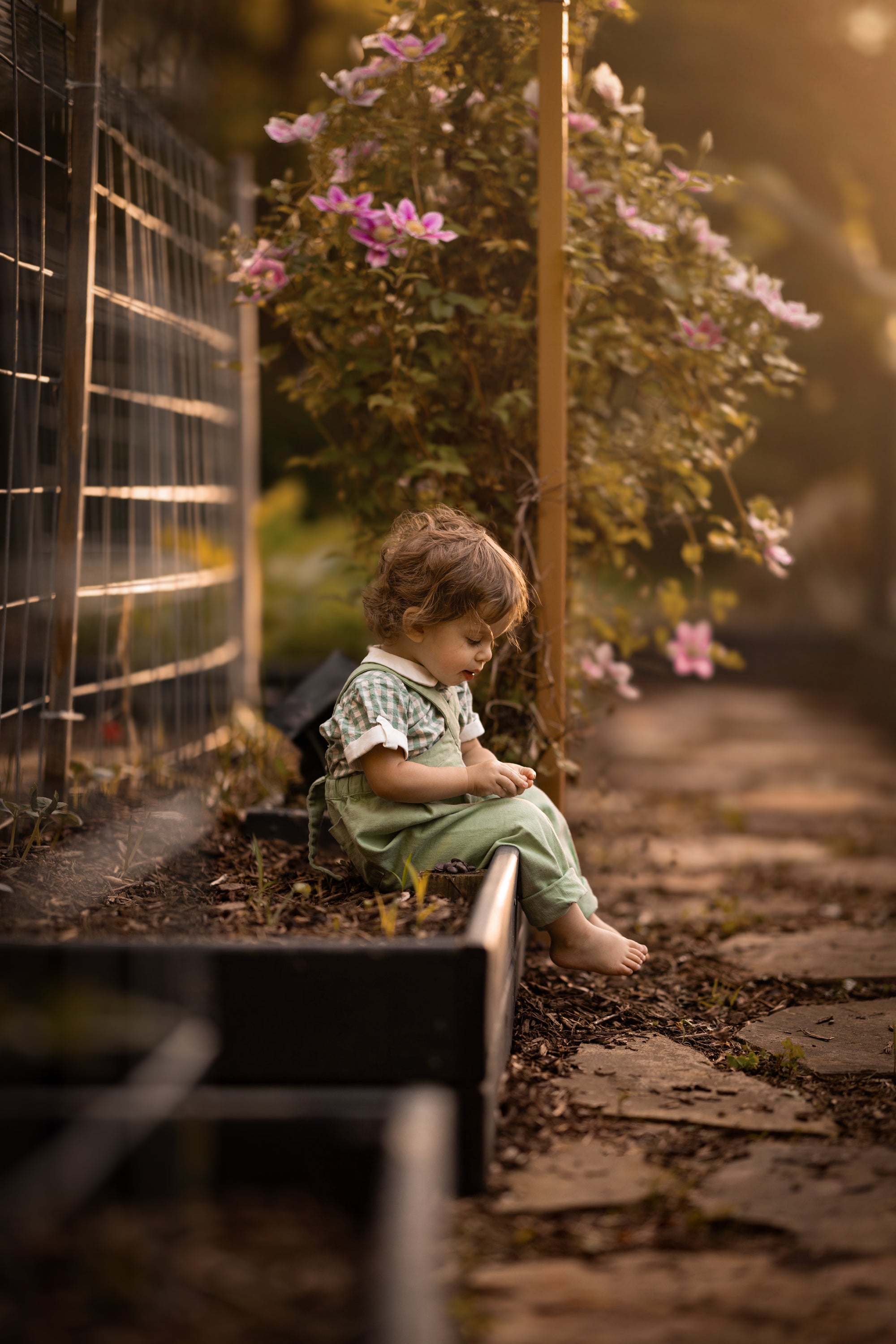 Child sitting on a stone path with flowers and a fence in the background