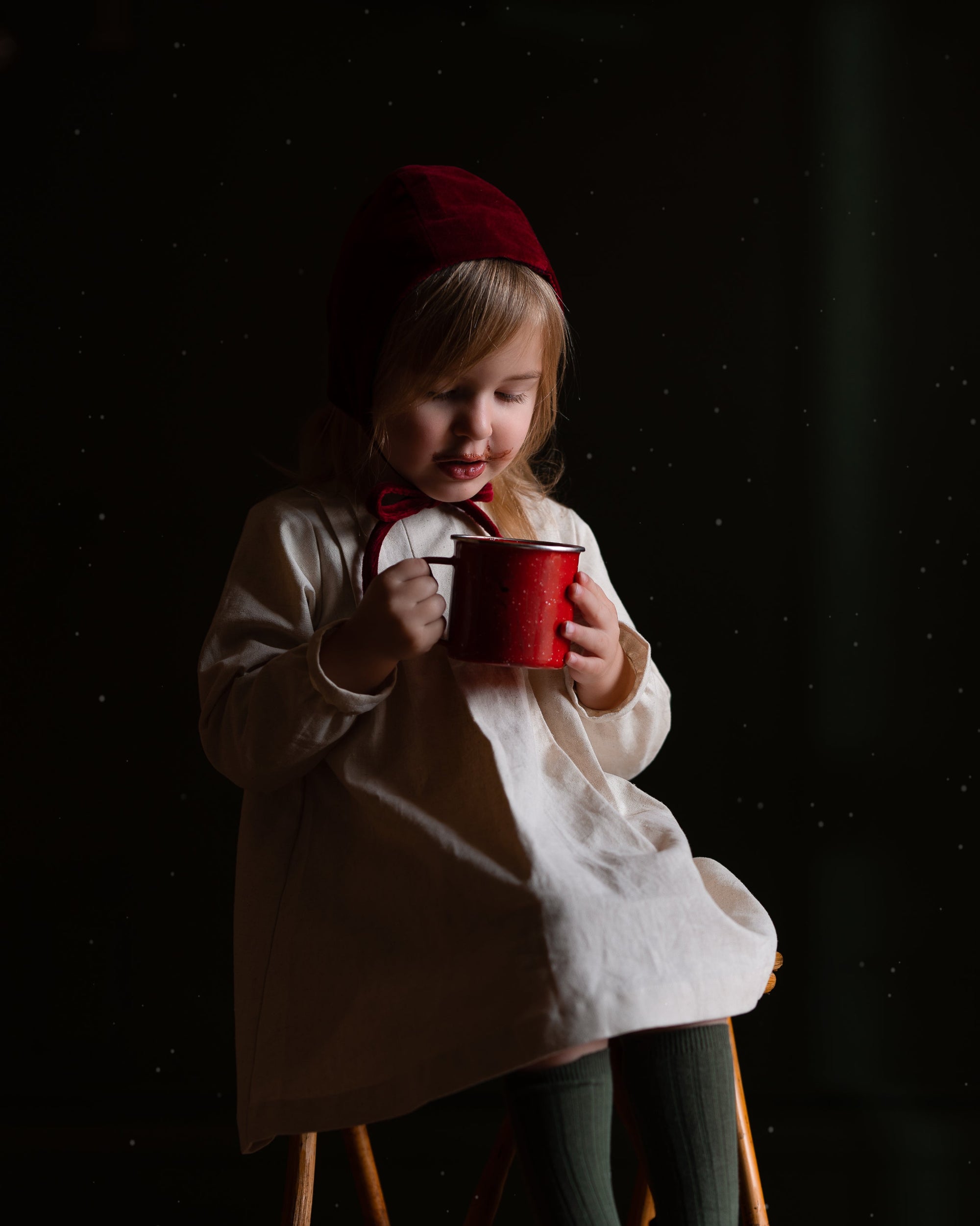 Child holding a red mug in a dark setting