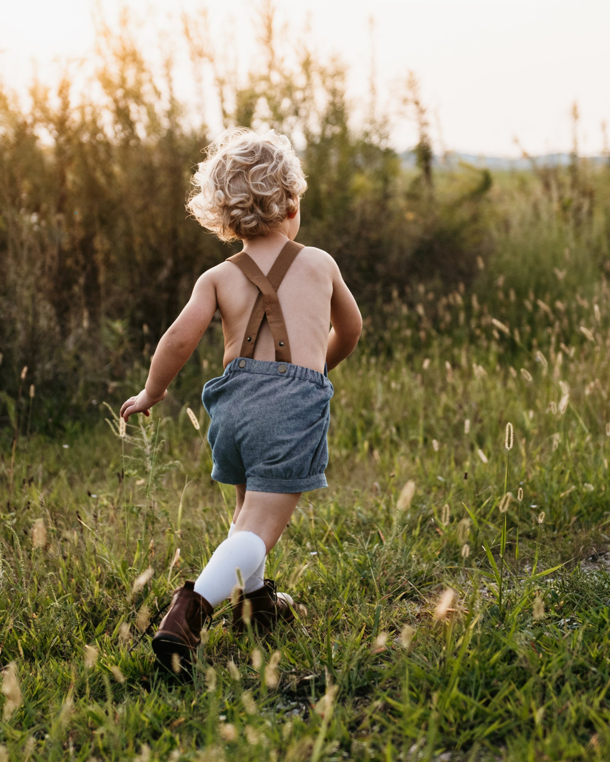 A playful 3-year-old boy running in chambray blue linen short overalls, showcasing the stylish design and comfort in action, perfect for playdates and family gatherings