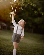 Child holding a toy airplane in a park with trees and sunlight filtering through.