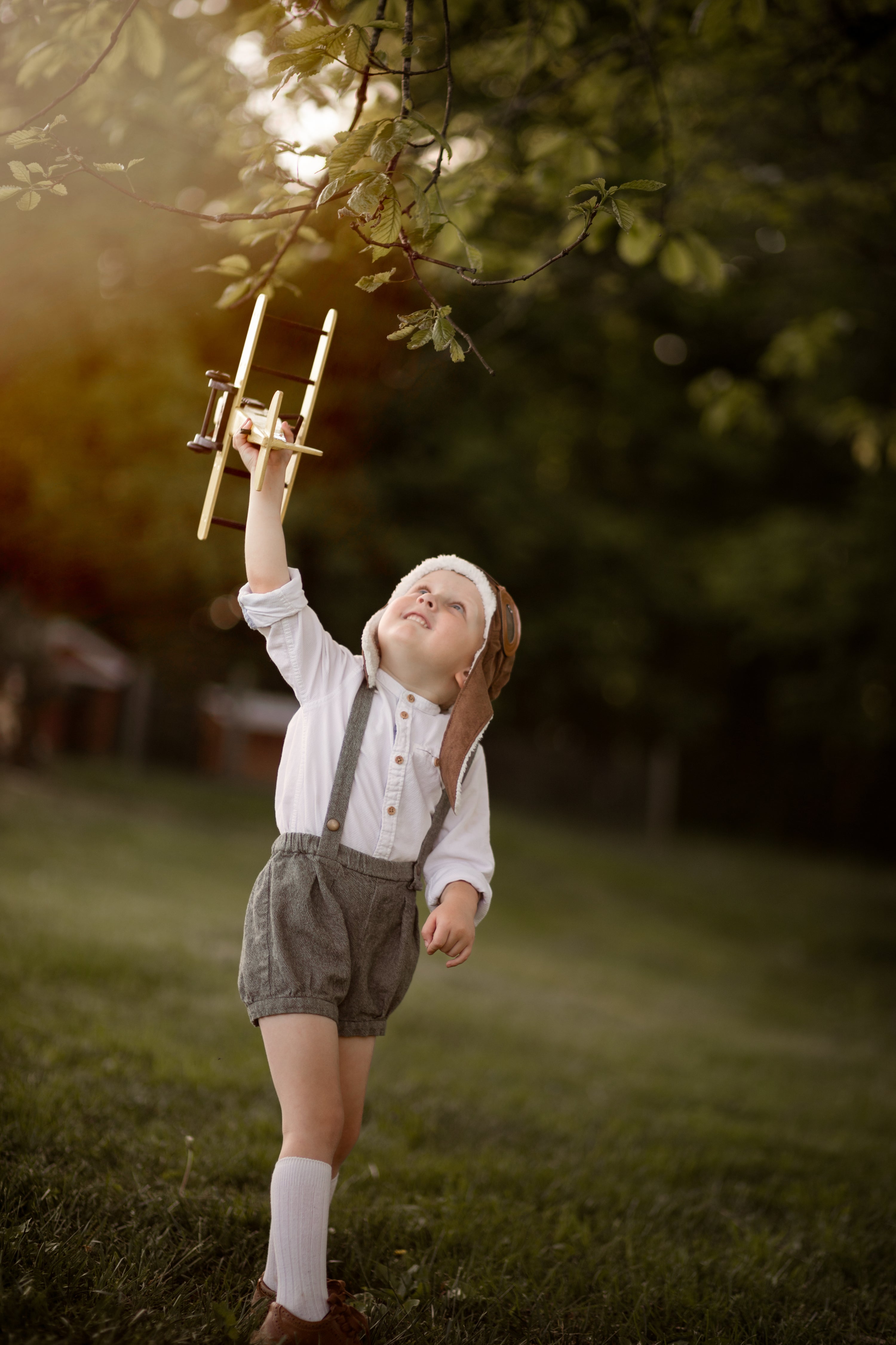 A 4-year-old boy wearing olive green linen suspender shorts, joyfully playing with a toy plane, highlighting the comfort and versatility of the shorts.