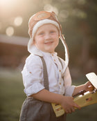 Child wearing a pilot hat and holding a toy airplane outdoors with a blurred background