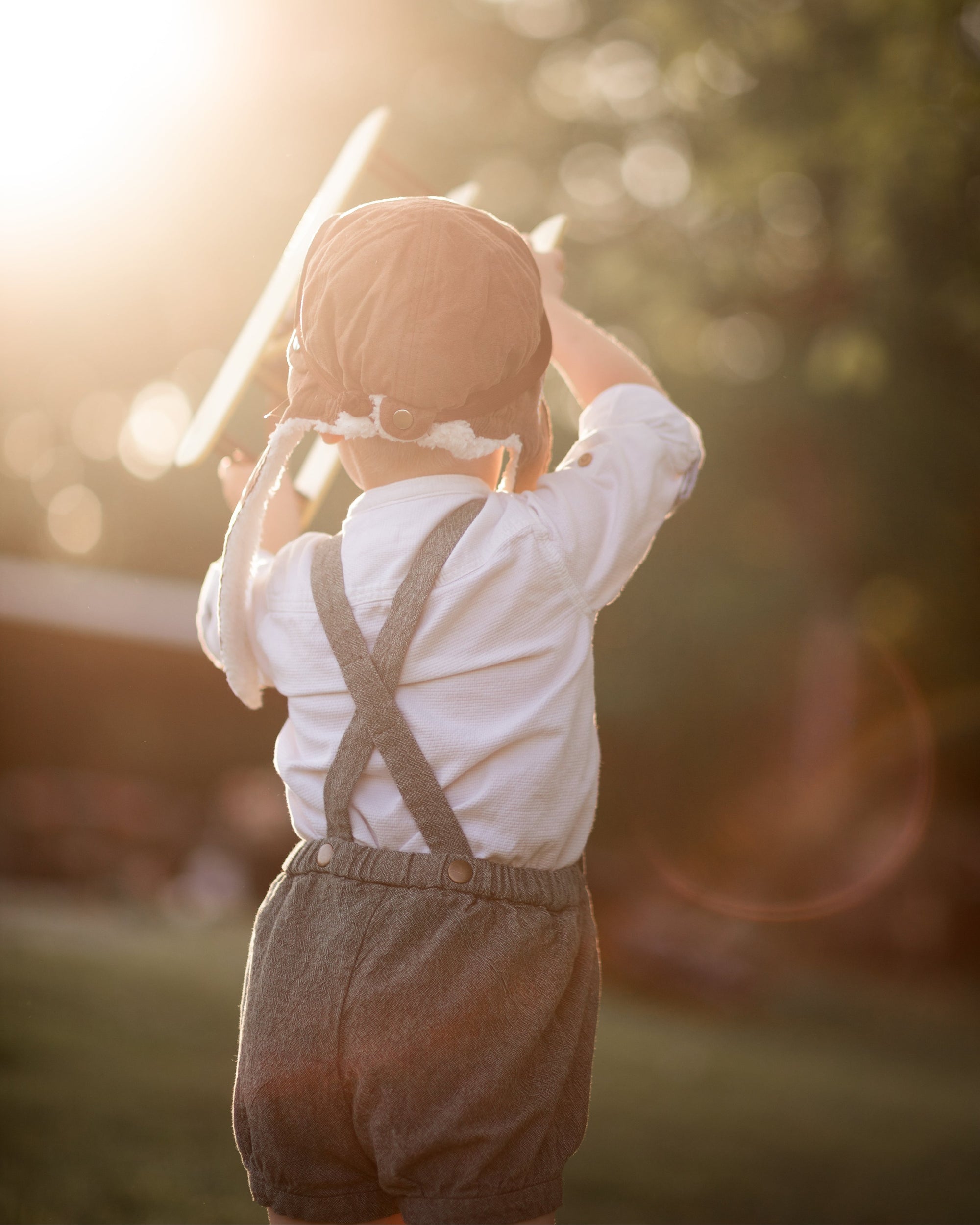 Child in suspenders playing with a toy airplane outdoors