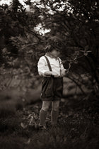 Black and white photo of a child in suspenders and shorts standing in a natural setting.