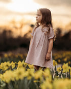 Young girl in a pink dress standing in a field of yellow flowers with a blurred background