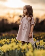 Young girl in a pink dress standing in a field of yellow flowers with a blurred background